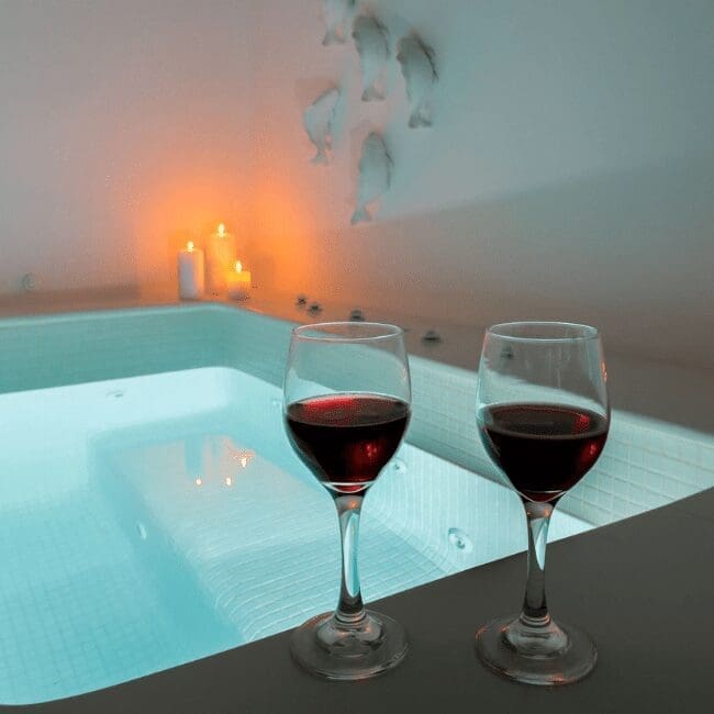 Two glasses of red wine beside a candlelit indoor hot tub in the Suite with Indoor Hot Tub