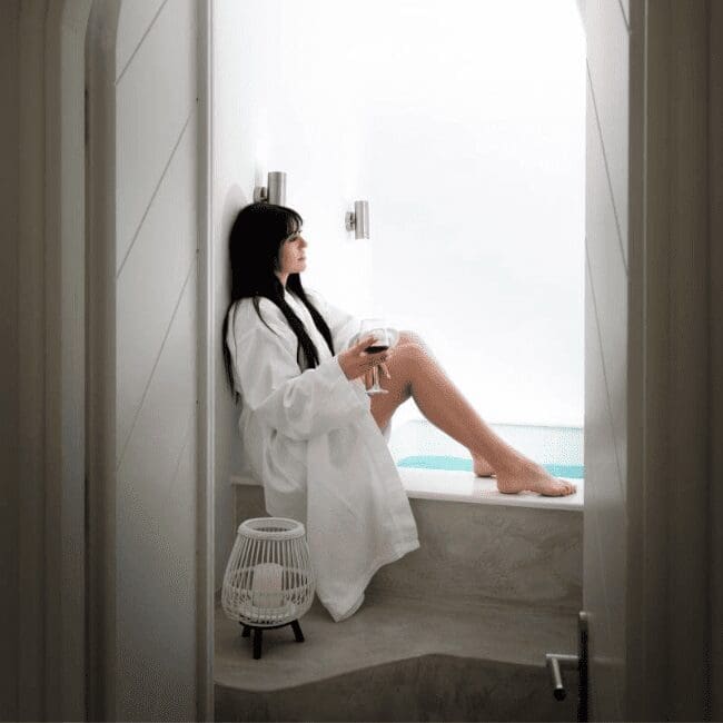 Guest in a white robe relaxing with a glass of wine on a window seat in an Executive Suite