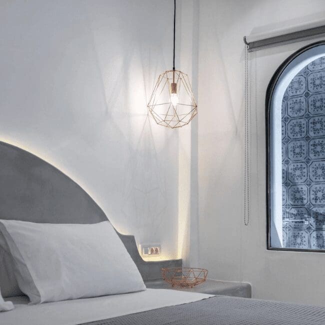Cycladic-style suite bedroom with rose gold pendant light and arched window at Emerald Collection Suites, Santorini