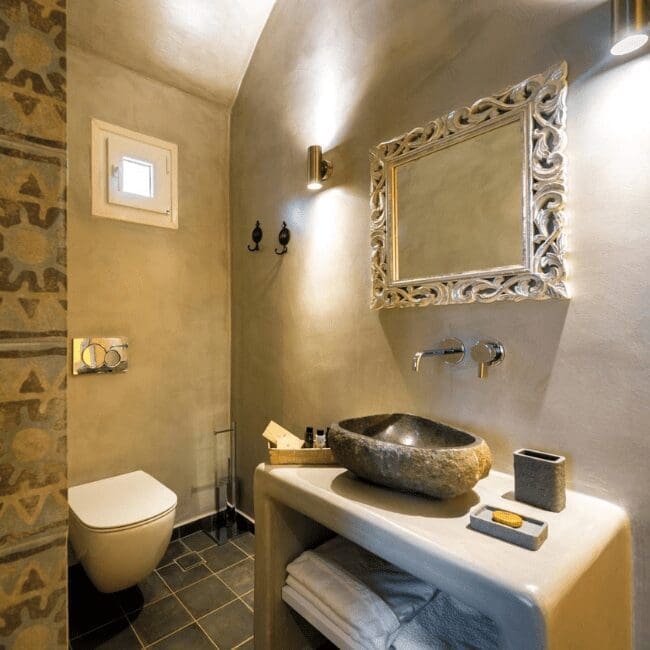 Boutique bathroom with stone sink, ornate mirror and vaulted ceiling in a suite at Emerald Collection Suites, Santorini