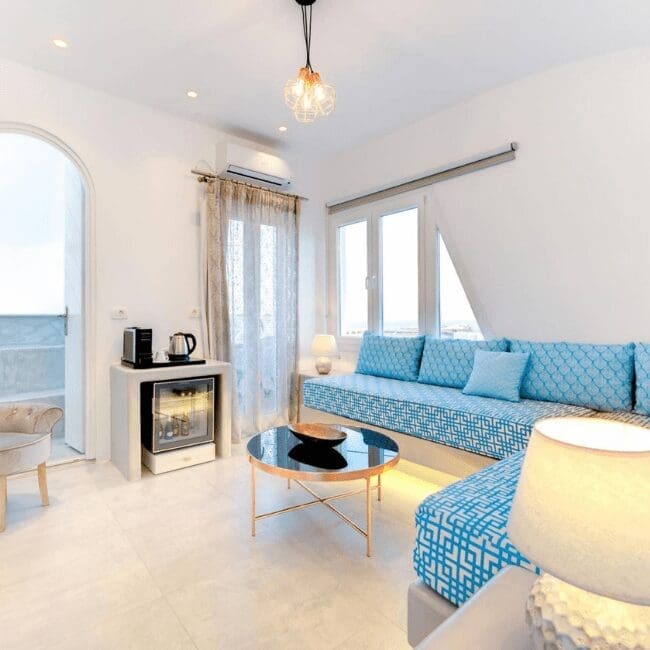 Bright suite living area with blue Cycladic furnishings, mini bar and balcony access at Emerald Collection Suites, Santorini