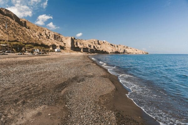 Exo Gialos Karterados beach with dark volcanic sand and a rocky headland, Santorini