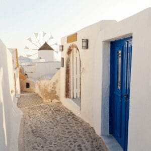 Narrow whitewashed alley with a blue door and windmill in Oia, Santorini