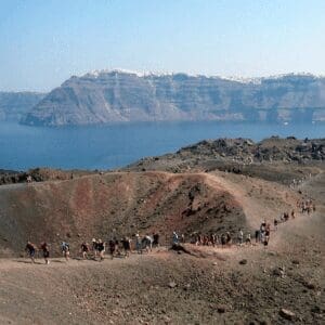 Visitors hiking the volcanic crater of Nea Kameni with the Santorini caldera cliffs beyond